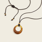 Seraphina Treasures Selenyra necklace with a translucent amber-toned hollow resin pendant on a black cord with gold bead accents.