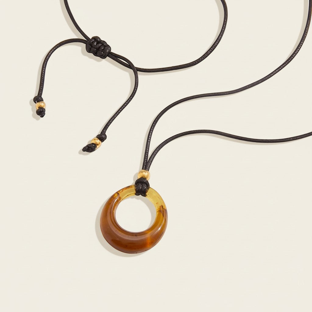 Seraphina Treasures Selenyra necklace with a translucent amber-toned hollow resin pendant on a black cord with gold bead accents.