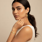 Seraphina Treasures Anthea gold-tone bracelet and hoop earrings set with sunburst designs. Model wears the jewelry with a cream dress.