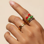 Seraphina Treasures gold ring with red cherry and green leaf design, and a second band with small clear stones.