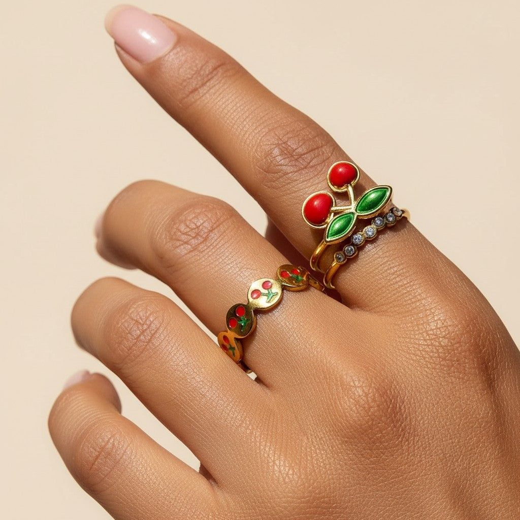 Seraphina Treasures gold ring with red cherry and green leaf design, and a second band with small clear stones.