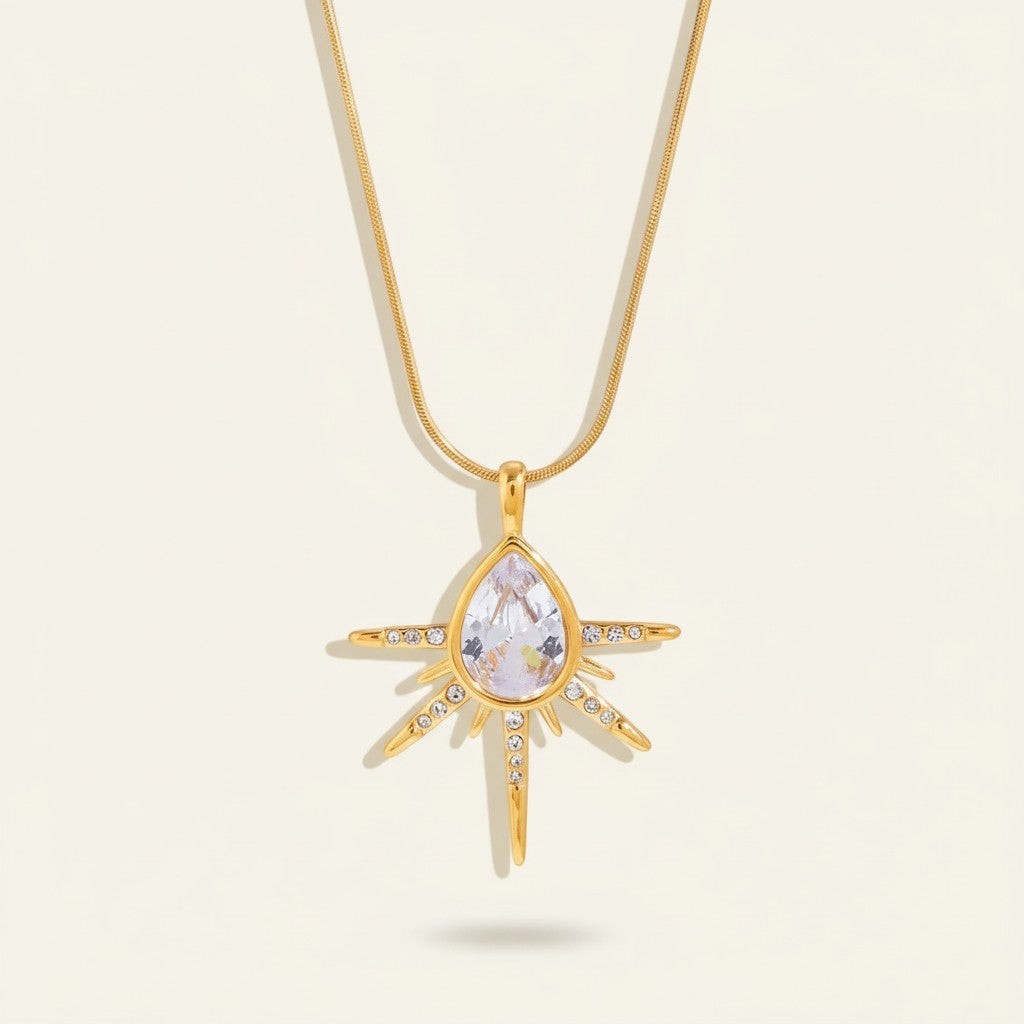 Seraphina Treasures gold necklace with a teardrop cubic zirconia pendant surrounded by starburst rays and small clear stones.