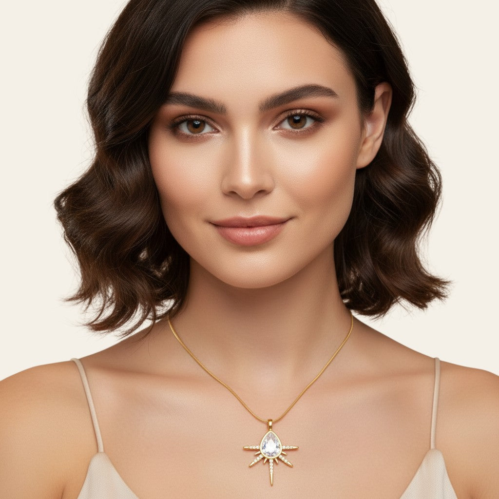 Seraphina Treasures gold necklace with teardrop cubic zirconia pendant surrounded by starburst rays and small clear stones.