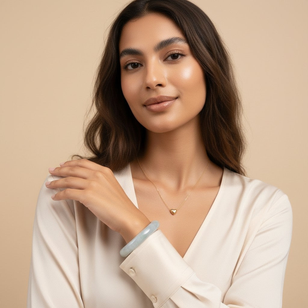 Seraphina Treasures gold heart pendant necklace on a delicate chain, worn by a woman with a jade bangle.