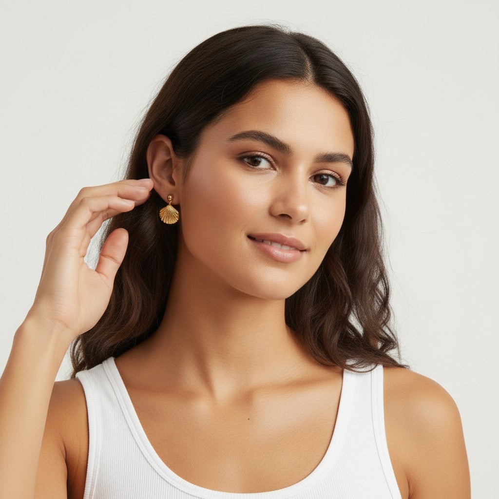 Seraphina Treasures gold shell drop earrings on a woman with dark wavy hair wearing a white tank top.