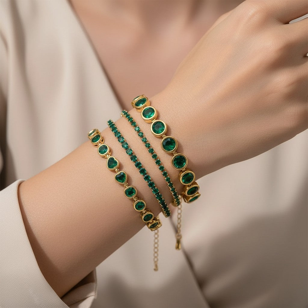 Seraphina Treasures gold chain bracelet with emerald green heart and round cut zirconia stones, and a gold beaded bracelet.