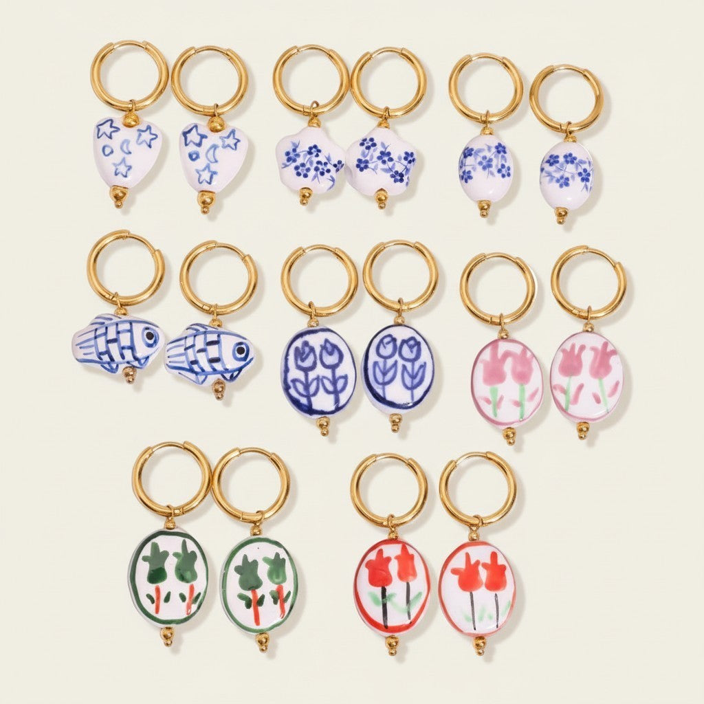 Seraphina Treasures Kyanis Earrings: assorted ceramic drop earrings with gold hoops, featuring blue floral, fish, pink tulip, green floral, and red tulip designs.