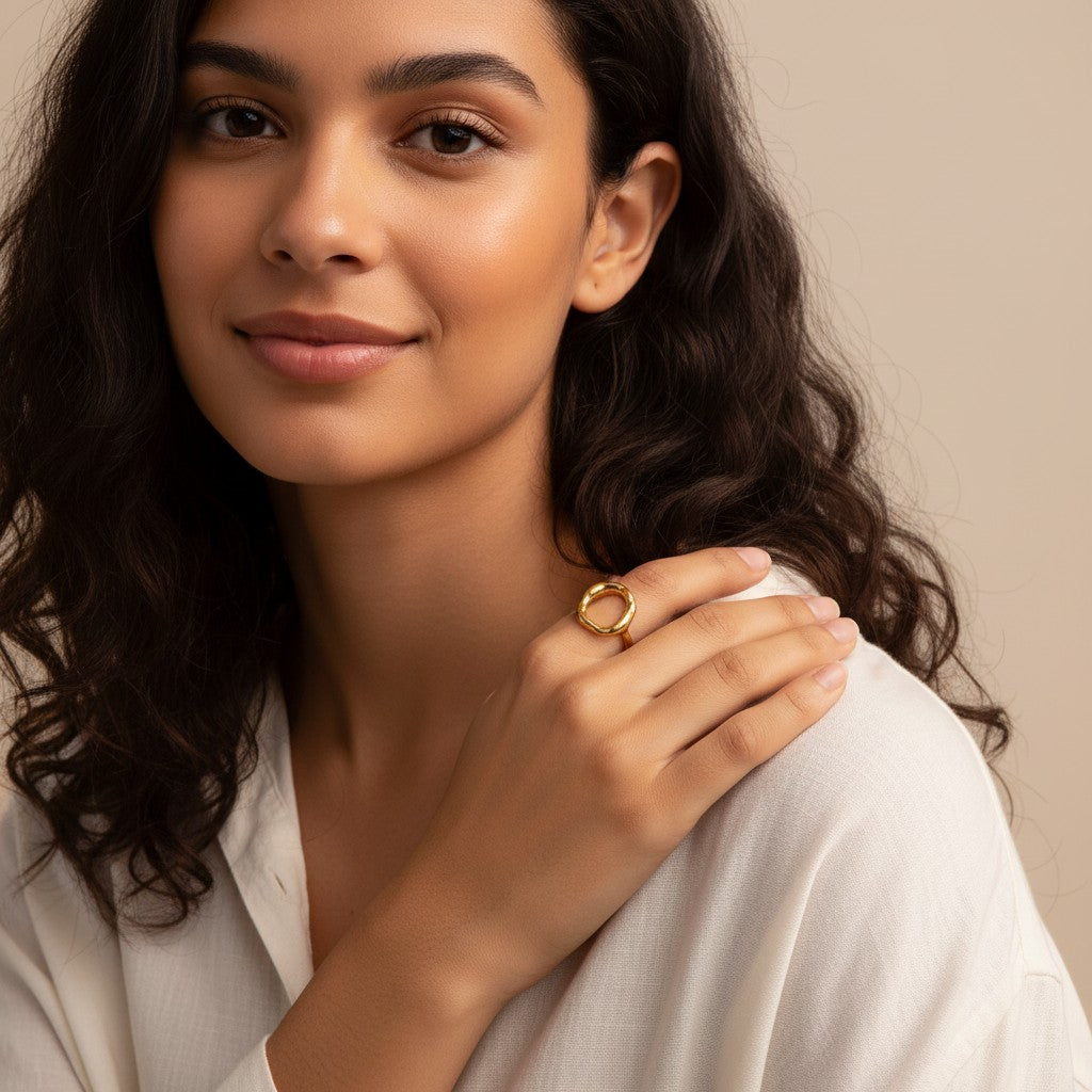 Seraphina Treasures Lava ring in gold with a hollow, organic circular design. Worn on a finger against a white shirt.