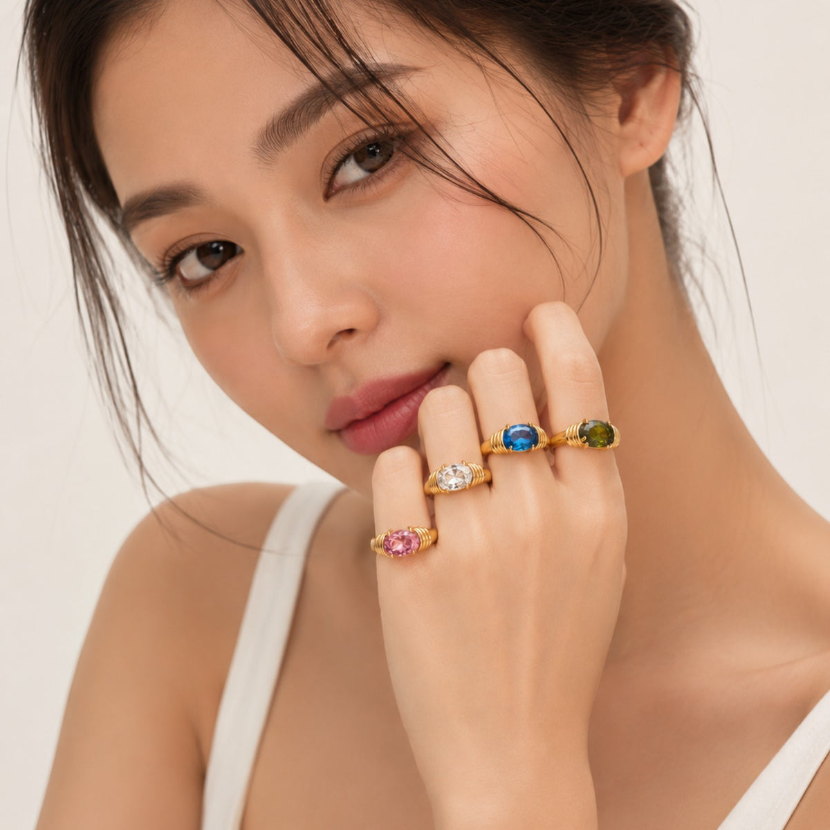 Seraphina Treasures Meliora rings with oval-cut gemstones in pink, clear, blue, and green set in gold-tone wire bands on a woman's hand.