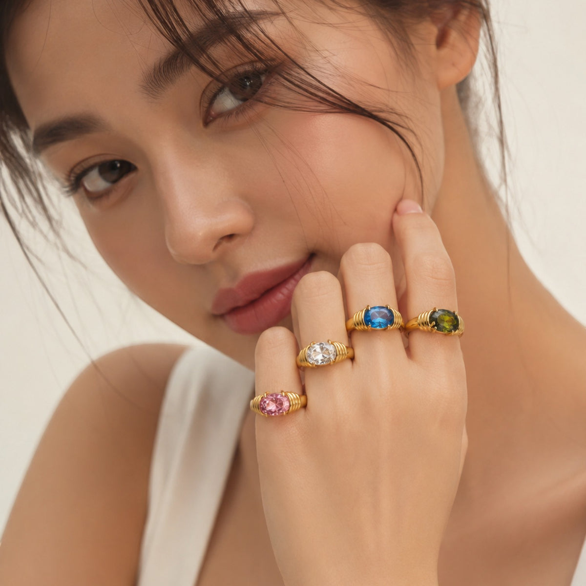 Seraphina Treasures Meliora rings featuring oval-cut gemstones in pink, clear, blue, and green set in gold-tone bands.