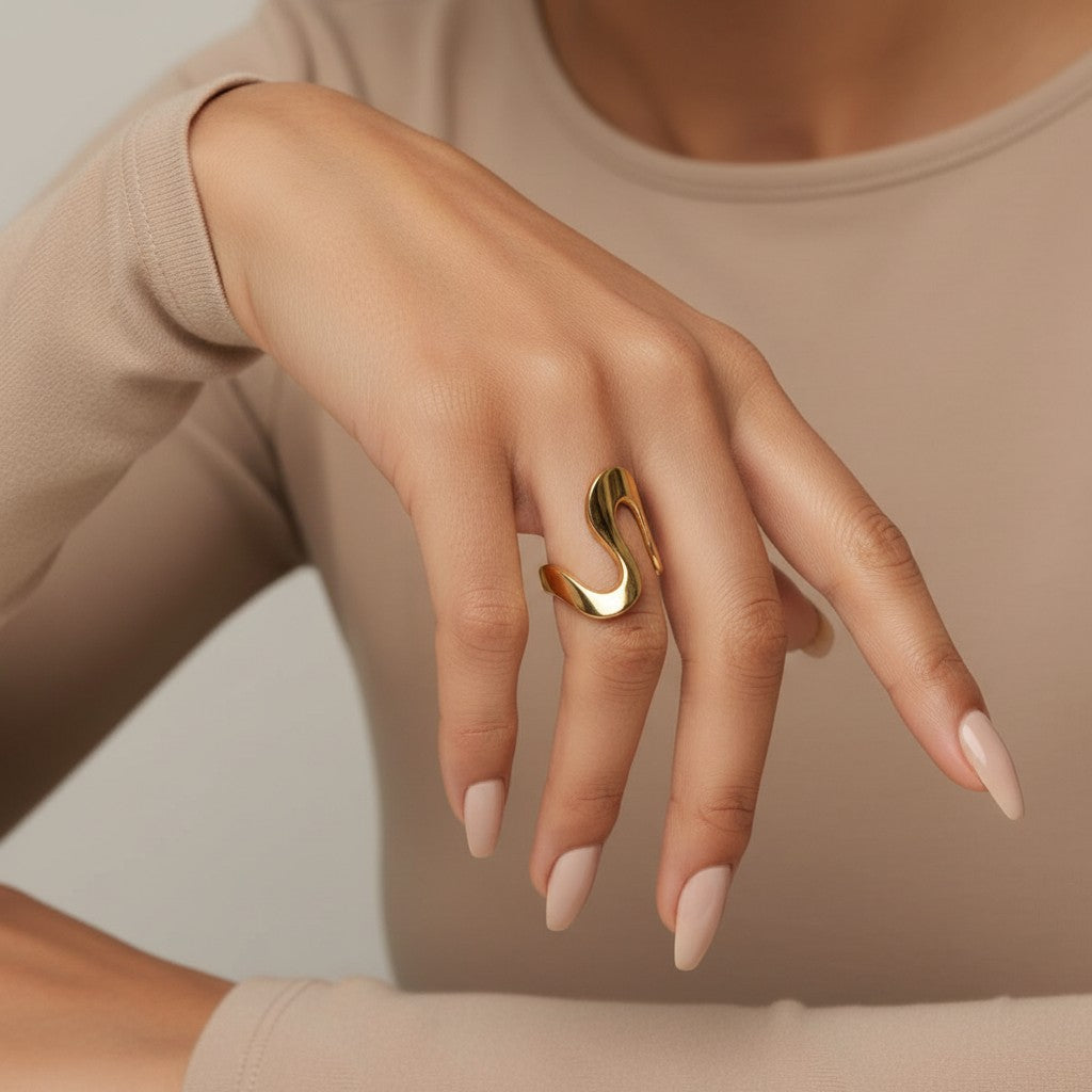 Seraphina Treasures Orvian gold abstract statement ring on a woman's finger with long nude nails and white shirt.