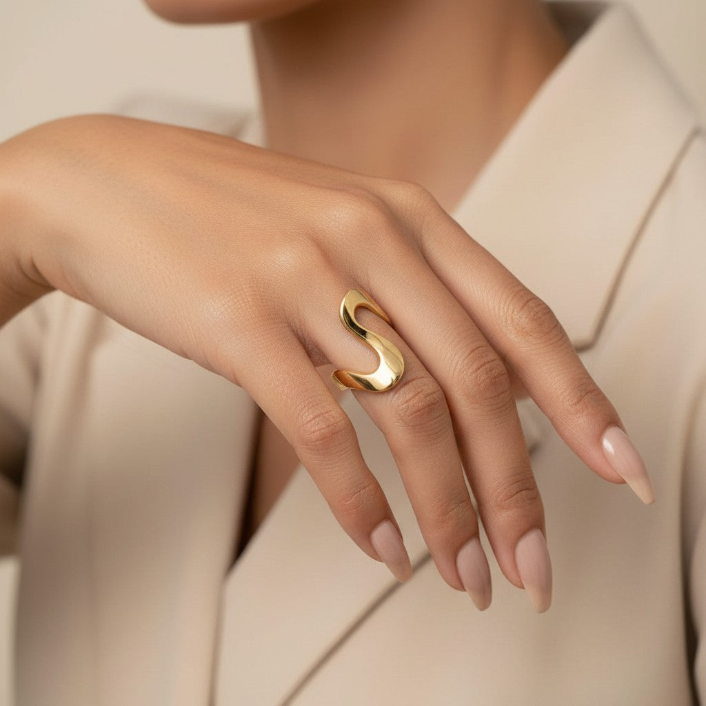 Seraphina Treasures Orvian gold abstract statement ring on a woman's finger with long nude nails.