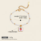 Seraphina Treasures Clytia bracelet with white pearls, gold beads, and a square pendant featuring a red strawberry. Adjustable length.