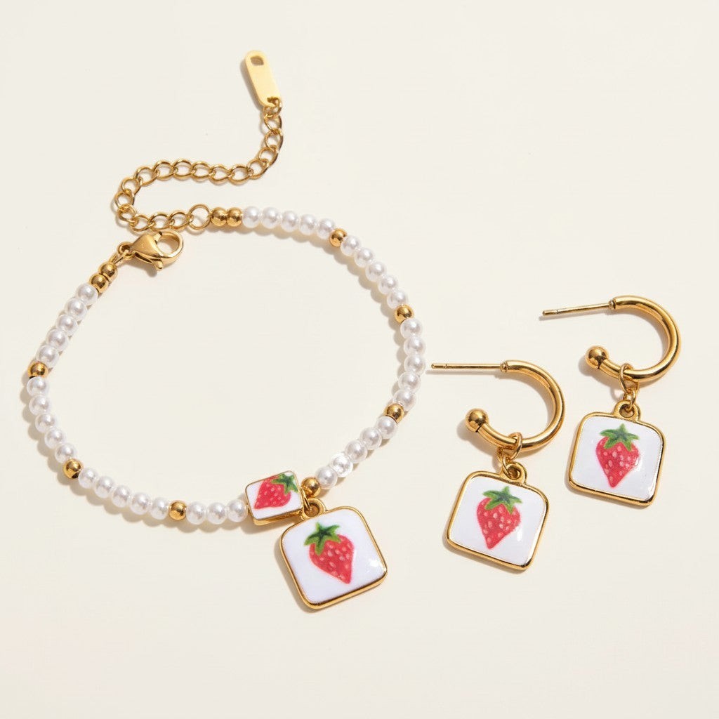 Seraphina Treasures Clytia bracelet and earring set with faux pearls, gold accents, and strawberry pendants on white squares.