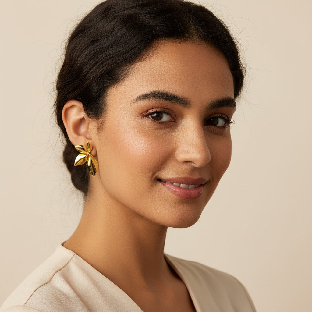 Seraphina Treasures Sylvara earrings in gold and silver tones, shaped like abstract leaves. A hand holds a gold earring near a silver one worn on an ear.